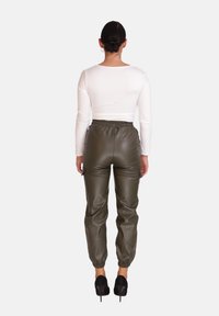 Groene neplederen cargobroek met een elastische tailleband en boorden, gecombineerd met een lange mouw witte top. Hoge zwarte hakken zichtbaar.