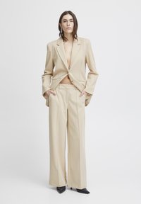 Beige tailored blazer and wide-leg trousers with a textured finish. Black pointed-toe heels. Minimalist design, front pockets, and single button.
