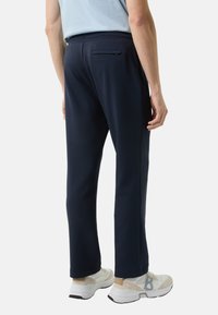 Granatowe spodnie dresowe z elastycznym pasem, posiadające tylną kieszeń, zwężane nogawki i miękką fakturę. Noszone z białymi butami sportowymi.