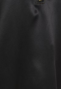 Tissu noir à texture lisse avec une légère brillance. Un accent doré en haut crée un contraste avec le fond.