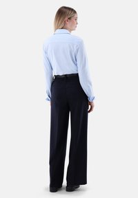 Hellblau gestreiftes Hemd mit Knöpfen und langen Ärmeln, kombiniert mit hochtaillierten schwarzen Hosen. Aus einem glatten Stoff mit maßgeschneiderter Passform.