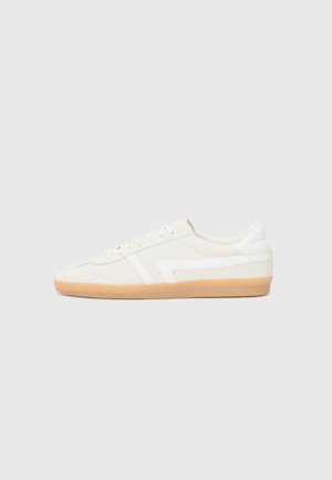 White sneakers with a suede and leather upper, featuring a gum rubber sole, stitched accents, and a minimalistic design.
