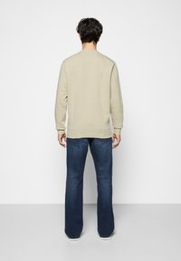 Felpa beige con scollo rotondo e maniche lunghe, abbinata a jeans svasati blu scuro, vista da dietro, con tessuti semplici.