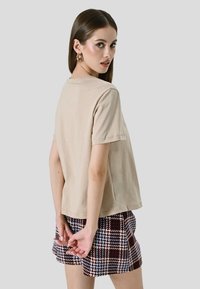 Beige katoenen t-shirt met korte mouwen, ronde halslijn en een relaxte pasvorm, gedragen met een geruite short met bordeauxrode en blauwe patronen.