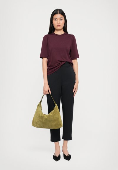 Burgundy t-shirt, black trousers, and black pointed flats. Holding a soft olive green suede shoulder bag with a curved shape.