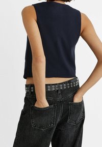 Marineblaues Cropped-Top mit ärmellosem Design, kombiniert mit hochgeschnittenen schwarzen Jeanshosen mit großen Gesäßtaschen und einem gep studierten schwarzen Gürtel.