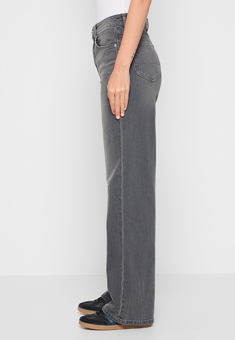 Jean large gris en denim, avec une taille haute, des poches latérales et une finition soignée. Associé à des baskets noires.