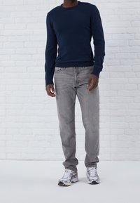Pull en maille bleu marine à col rond, associé à un jean gris clair et des chaussures de sport argentées. Tissu texturé, coupe ample.