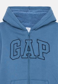 Blå fleecefodrad hoodie med framdragskedja och "GAP"-logotyp broderad över bröstet.