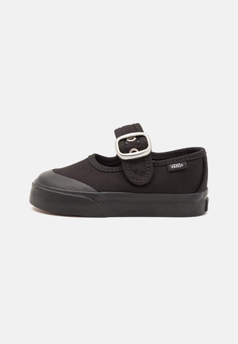 Melnas Vans slip-on kurpes ar gumijas zoli, noapaļotu pirkstu daļu un regulējamu sprādzi uz augšas.