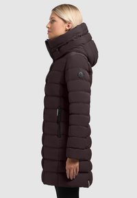 Giubbotto imbottito in un intenso bordeaux scuro con colletto alto, chiusura con zip sul davanti e tasche laterali. Presenta un design trapuntato e un'etichetta con logo sulla manica.