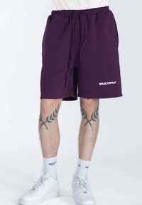 Shorts de sport violets avec une taille élastique et un cordon de serrage, dotés de poches latérales et d'un logo "MULTIPLY" blanc à l'ourlet.
