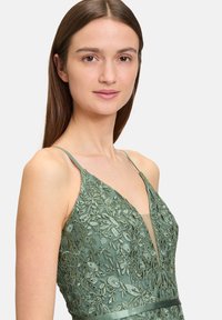 Grünes Spitzenkleid mit floralem Stickereien, V-Ausschnitt-Design und dünnen Trägern. Verfügt über einen strukturierten Stoff und eine figurnahe Silhouette.