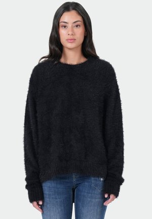 Un pull noir en peluche avec un col rond et des manches longues, avec des bords côtelés aux poignets et à l'ourlet. Associé à un jean bleu.