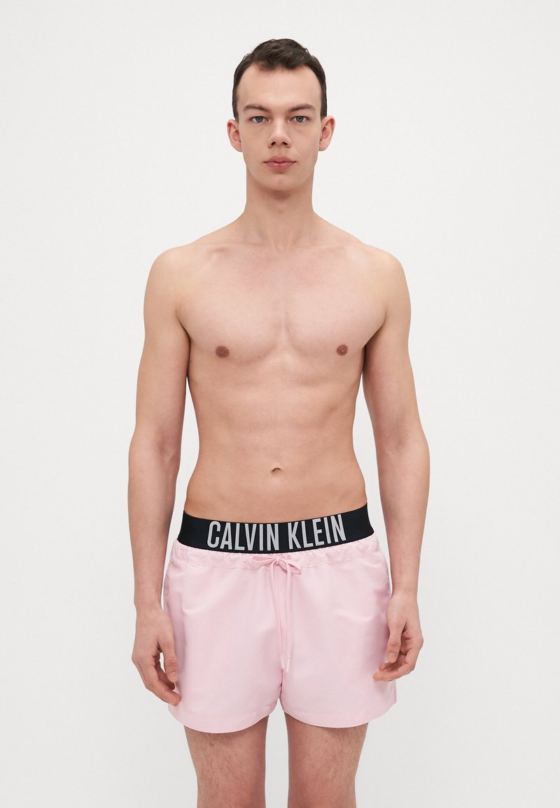 Rosa Badehose mit einem schwarzen Calvin Klein Logo-Bund, ausgestattet mit einem Kordelzug, glatter Textur und in Kniehöhe.