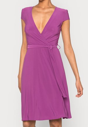 Robe portefeuille violette avec manches courtes, encolure en V et ceinture nouée à la taille, portée par une personne sur un fond uni.
