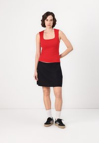 Top de tiro ajustado rojo combinado con una falda negra, usado con zapatillas negras y calcetines blancos. Tejido suave, diseño minimalista y estilo casual.