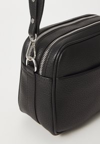 Borsa a mano in pelle nera con due zip argento, superficie testurizzata, una tracolla rimovibile e forma rettangolare. Dettagli in metallo argentato.