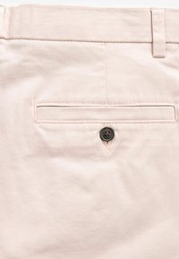 Pantalones de tela rosa claro con una textura suave, que cuentan con un bolsillo trasero con un botón oscuro y un detalle de costura minimalista.