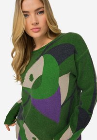 Maglione verde e beige con motivo a fantasie e dettagli viola, caratterizzato da una vestibilità rilassata, maniche lunghe e un tessuto a maglia testurizzata.