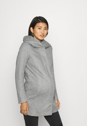 Grey wool coat with a wide, fold-over hood, vertical seams, and long sleeves, paired with black pants. Smooth texture and tailored fit.