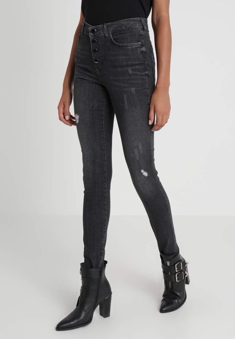High-waisted black skinny jeans with button fly, distressed details, and slight fading. Worn with black ankle boots featuring buckles.