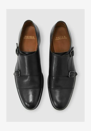 Pantofi negri din piele cu un design elegant, accentuati de două catarame, textură netedă și vârf rotund. Logo-ul brandului este vizibil în interior.