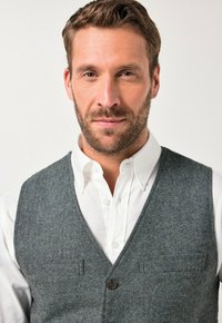 Graham Weste aus Wolle mit einem V-Ausschnitt, die über einem weißen Hemd mit Knöpfen getragen wird und zwei vordere Taschen sowie eine Knopfleiste aufweist.