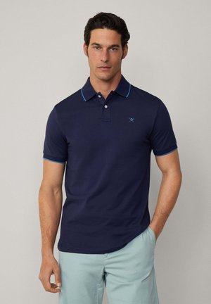 Marineblauw poloshirt van zachte stof met lichtblauwe bies op de kraag en mouwen, voorzien van een klein geborduurd logo op de borst.