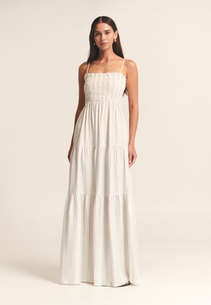 Maxi dress in light fabric with thin straps, smocked bodice, tiered skirt, and subtle vertical stripes in white and beige.