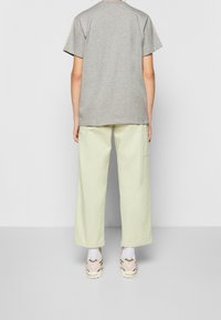 Grå bomulls t-shirt med kort ärm, kombinerad med ljusgröna vida byxor och beige sneakers med detaljer.