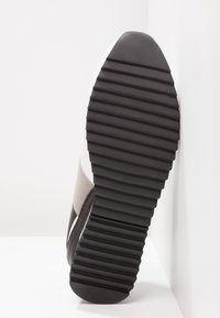 Platt skosula med svart gummi, texturerade räfflor för grepp. Har ett vitt ovandel med grå tygdetaljer, rundad tådesign.