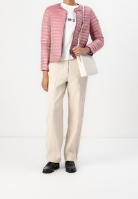 Rosa kviltad jacka, vit tröja med text, beige vida byxor och svarta skor. Tillbehör inkluderar en liten vit handväska.