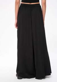 Zwarte wijde broek met een losse pasvorm, voorzien van een elastische tailleband en een gladde textuur, elegant naar de vloer vallend.