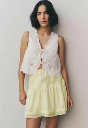 Witte geborduurde crop top met golvende randen, gecombineerd met een lichtgele flared jurk met textuurbanden en kanten accenten.