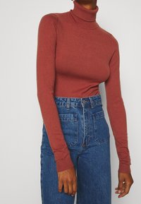 Rustkleurige coltrui met lange mouwen, gebreide textuur. Gecombineerd met hooggetailleerde blauwe denim jeans met voorzakken.