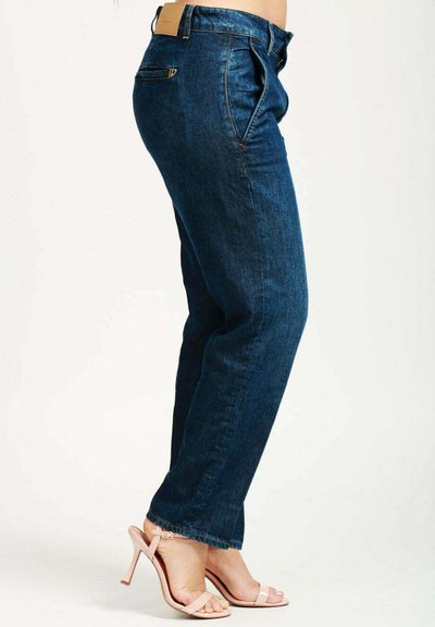 Jeans in denim blu scuro con design a gamba dritta, leggere sfumature e un'etichetta beige sulla vita posteriore. Indossati con sandali rosa chiaro.