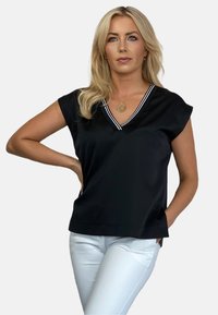 Czarna bluzka z krótkimi rękawami, dekolt w serek akcentowany białymi paskami, gładki materiał, w połączeniu z białymi spodniami, dopasowany krój.