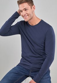 Tamnosivi majica dugih rukava od mekog materijala, s okruglim izrezom i glatkom teksturom, nosi se s tamnoplavim trapericama.