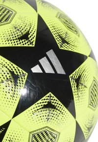 Pallone da calcio nero e giallo neon con motivi esagonali, superficie testurizzata e logo Adidas argentato su un lato.