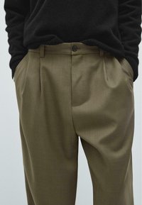 Olive green pleated trousers with a relaxed fit, made from soft fabric; features a single button closure and side pockets.