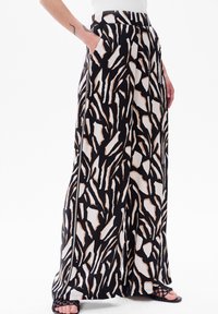 Wijdere broek in een zwart, wit en beige abstract patroon; voorzien van zijzakken en een gladde stoftextuur.