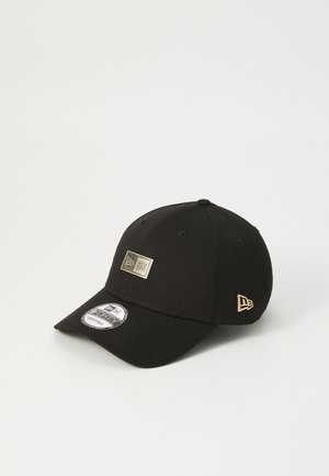 Cappellino da baseball nero realizzato in tessuto, con un badge logo dorato sul davanti e un piccolo accento del logo sul lato. Visiera curvata e design a sei pannelli.