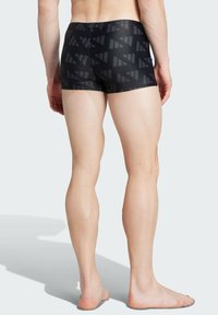 Čierne plavecké šortky s geometrickým vzorom v rôznych odtieňoch šedej, vyrobené z elastického materiálu, s priliehavým strihom a dĺžkou po strednú časť stehna.