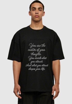 Oversized black t-shirt featuring white cursive text and a logo. Soft fabric, wide sleeves, and a round neckline.