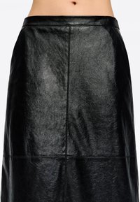 Falda de cuero negra con una textura suave y brillante. Presenta una cintura ajustada y líneas limpias, destacando un diseño minimalista.