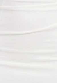 Bílé šaty s přiléhavým střihem, vyrobené z měkké, texturované látky a s vertikálními sklady, které vytvářejí jemné záhyby po celém oblečení.