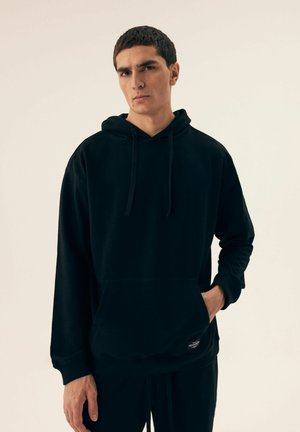 Black cotton hoodie with a front pocket, drawstring hood, and ribbed cuffs. Simple design and smooth texture.