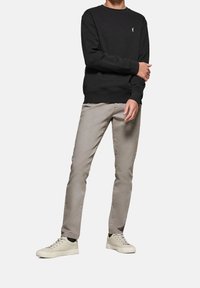 Černá mikina s kulatým výstřihem, šedé slim-fit kalhoty a béžové tenisky. Mikina má na hrudi malé logo.