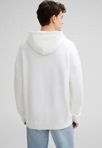 Witte hoodie met een gestructureerde stof, losse pasvorm, verlaagde schouders en geribbelde manchetten; heeft een grote, zachte capuchon.
